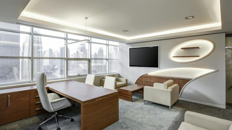 gray office rolling chair near brown wooden desk in front of flat screen tv on white painted wall